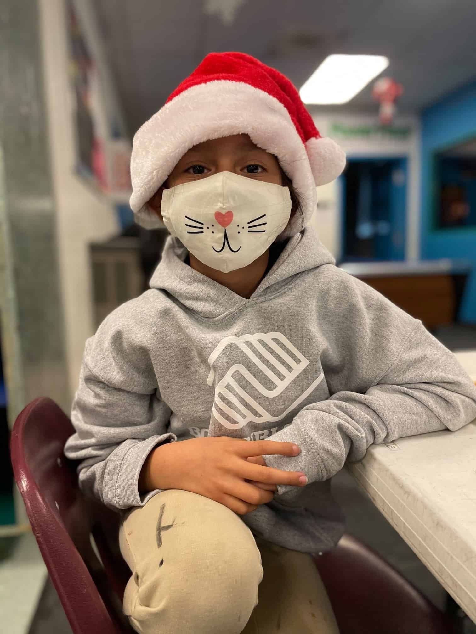 Child member of BGCTM wearing a cat mask and Santa hat